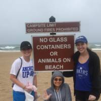 3 female students pose with a sign at Grand Haven Beach